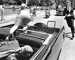 Kennedy mortalmente herido mientras Jackie trata de salir del coche y  un custodio se abalanza hacia el auto presidencial.